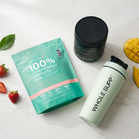 The Whole Supp Ultimate Starter Pack features a strawberry shake meal mix, black Elevate tub, white shaker bottle, alongside sliced mango, spinach leaves, and strawberries on a white surface.
